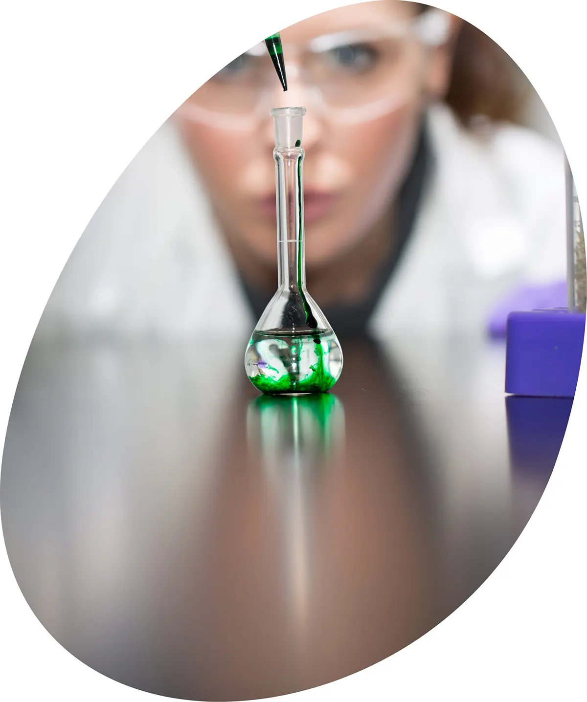 Female scientist adding green drops into a beaker